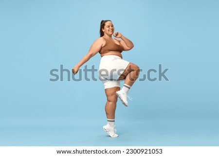 Young, positive, smiling overweight woman training in sportswear, running, doing cardio exercises against blue studio background. Concept of sport, body-positivity, weight loss, body and health care