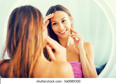 Young Positive Spanish Woman Examining Her Face By Looking At It In Mirror