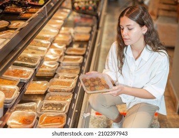 Young Positive Woman Choosing Ready Meal In Plastic Container At Supermarket