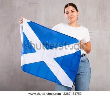 Young positive woman holding national flag of Scotland in her hands