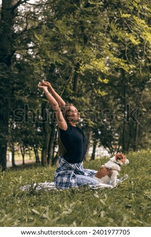 A young positive woman practicing yoga with a Jack Russell terrier dog, enjoying happy moments together while walking in the park on a summer day.