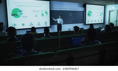 Young Postgraduate PhD Student Giving a Renewable Energy Lecture to Diverse Multiethnic Group of Women and Male Scholars in Dark College Room. Projecting Slideshow with Different Types of Green Energy - Powered by Shutterstock