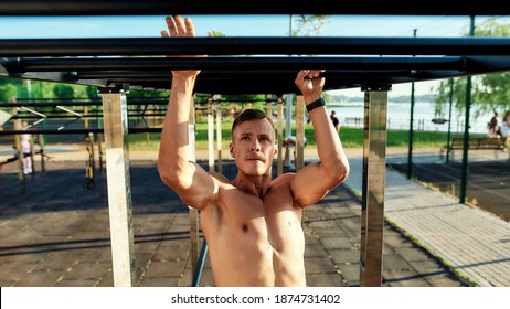 Young Powerful Caucasian Athlete With Naked Muscular Torso Swinging On Monkey Bars During Street Workout On Sport Ground, Widescreen. Crossfit, Healthy Lifestyle And Street Sport Concept