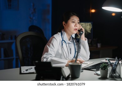 Young Practitioner Doctor Working At 24h Open Clinic. Asian Japanese Female Nurse Answering Phone Calls In Late Night Hospital. Medical Staff Discussing And Solve Problem In Dark Workplace Midnight