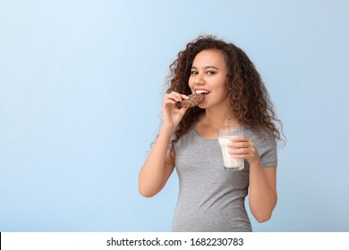 Young pregnant African-American woman with milk and cookie on color background
