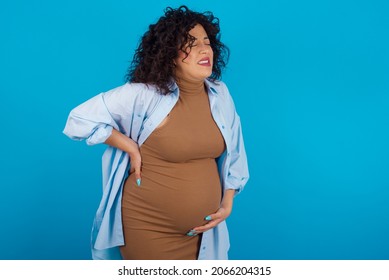 Young Pregnant Arab Woman Standing On Blue Studio Background  Suffering Of Backache, Touching Back With Hand, Muscular Pain