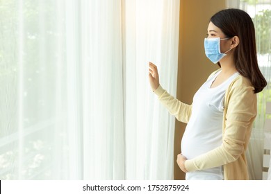 Young Pregnant Asian Woman In Medical Mask Stay Alone At Home For Self Quarantine. Home Quarantine, Prevention Covid 19, Coronavirus Outbreak Situation Concept Pregnancy Mother Looking Through Window 