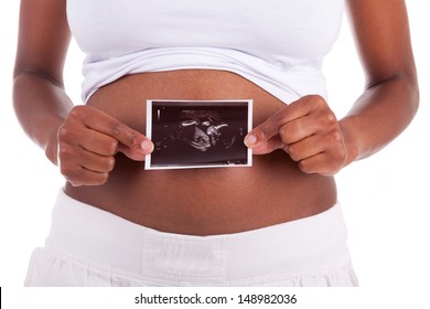 Young pregnant black woman holding an ultrasound picture in front of  her belly , isolated on white background - African people