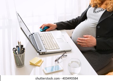 Young pregnant business woman sitting at the desk and working on the laptop.