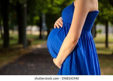 Young pregnant caucasian woman closeup with no face standing outdoors on sunny day holding her belly wearing blue summer dress.tif