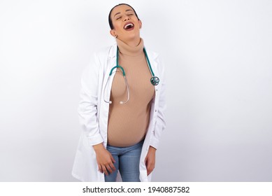 Young Pregnant Doctor Woman Wearing Medical Uniform Against White Background With Broad Smile, Shows White Teeth, Feeling Confident Rejoices Having Day Off.