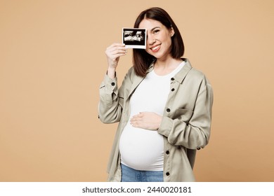 Young pregnant expectant woman future mom wear grey shirt with belly stomach tummy with baby hold cover eye with ultrasound image isolated on plain beige background. Maternity family pregnancy concept - Powered by Shutterstock