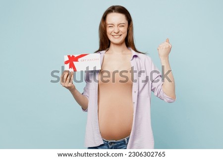 Young pregnant future mom woman with belly tummy with baby wear casual clothes hold gift coupon voucher card for store do winner gesture isolated on plain blue background. Maternity pregnancy concept