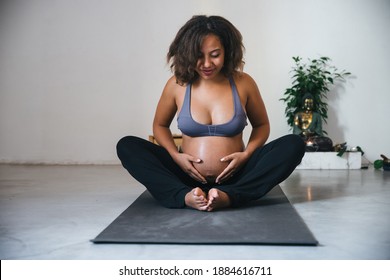 Young pregnant millennial woman sitting on the mat touches her belly after performing prenatal and meditation exercises at a yoga class - Concept of life and maternity - Shutterstock ID 1884616711