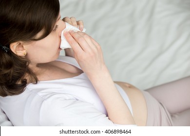 Young Pregnant Model Sitting On Bed And Wiping Her Nose With Tissue. Future Mom In Her Early Pregnancy Caught Cold Or Suffering From Allergy