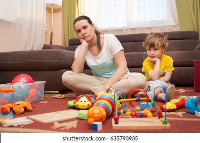 Young pregnant mother and her little son, at home. Mother and little son  sit on a floor. Mom tired to tidy up the house. Child scattered toys. Mess in the house. Mother has quarreled with the son.