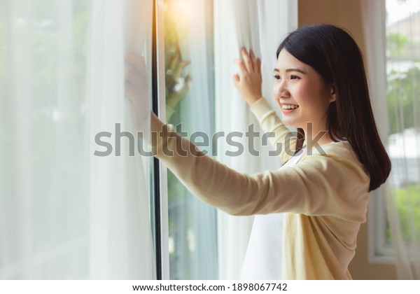 Young pregnant mother wake up in early morning open\
curtain looking at nice view feeling freshness with smile face and\
happiness at home. Attractive single mom stay alone in house,\
feeling relax 