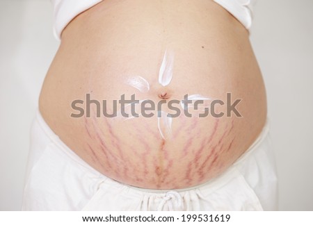 Young pregnant woman applying moisturizer on her belly.