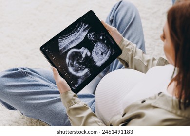 Young pregnant woman with belly wear casual clothes hold tablet pc computer with ultra sound image sit floor stay at home hotel flat rest relax spend free time in living room indoor. Maternity concept - Powered by Shutterstock