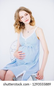 Young, pregnant woman in blue dress on white background. Pregnancy and motherhood. Fashion for pregnant women.