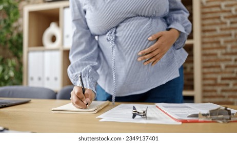 Young pregnant woman business worker writing on notebook touching belly at office - Powered by Shutterstock