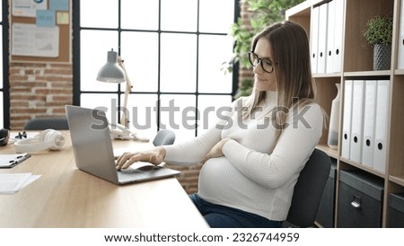 Young pregnant woman business worker using laptop touching belly at office