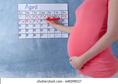 Young Pregnant Woman Counting Days With Calendar To Baby Birth On Color Wall