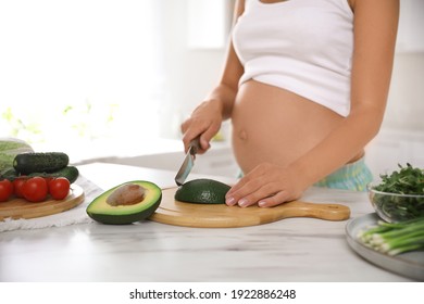 Young pregnant woman cutting avocado at table in kitchen, closeup. Taking care of baby health - Powered by Shutterstock