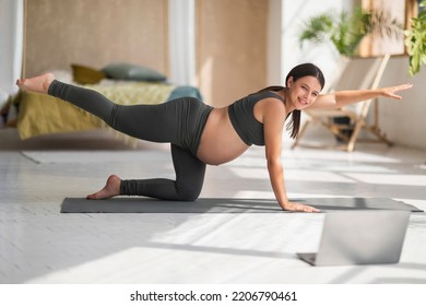 Young pregnant woman doing pilates in front of laptop at home, smiling millennial lady expecting baby training on fitness mat in living room, watching online tutorials and making pregnancy gymnastics - Powered by Shutterstock