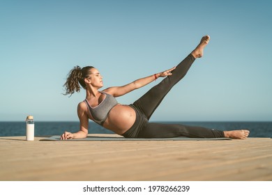 Young pregnant woman doing prenatal pilates exercises session next the sea - Health lifestyle and maternity concept