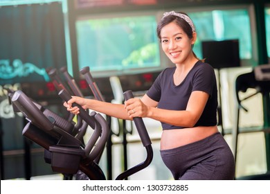 Young pregnant woman in fitness clothes exercising exercising on the elliptical cross trainer machine in fitness room with smiling and looking at camera.  - Powered by Shutterstock