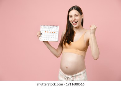 Young pregnant woman future mom in basic top with belly stomach tummy with baby holds female periods calendar isolated on pastel pink background studio. Maternity family pregnancy expectation concept