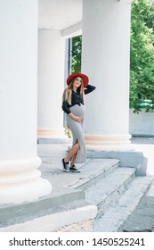 
young pregnant woman girl in a red hat striped dress pregnant belly waiting for a child beautiful long blonde hair walks around the city smiling