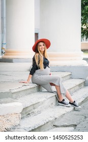 
young pregnant woman girl in a red hat striped dress pregnant belly waiting for a child beautiful long blonde hair walks around the city smiling