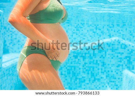 Young pregnant woman in green bikini swimming in pool. Underwater shot