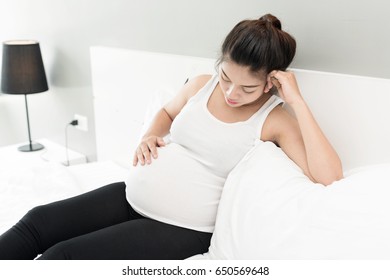 young pregnant woman having a headache and she is lying on the bed holding her belly and forehead - Powered by Shutterstock