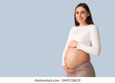 Young pregnant woman with heart made of cream on her belly against blue background - Powered by Shutterstock