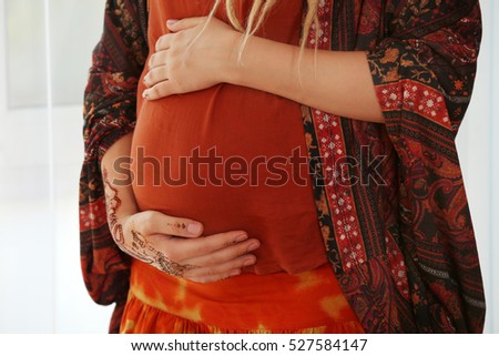 Young pregnant woman with henna tattoo on hand on light background