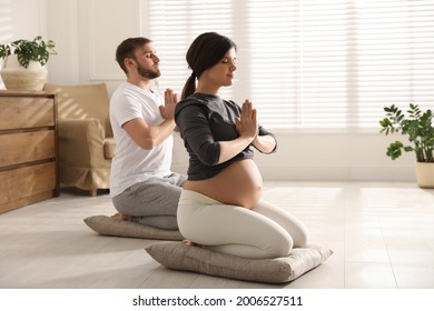 Young pregnant woman with her husband practicing yoga at home - Powered by Shutterstock