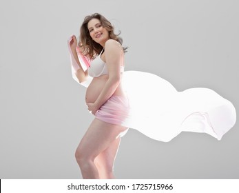 Young pregnant woman holding pink material in studio, smiling - Powered by Shutterstock