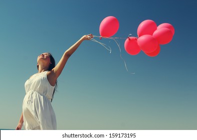 Young pregnant woman holding red balloons. Photo in old color image style. - Shutterstock ID 159173195