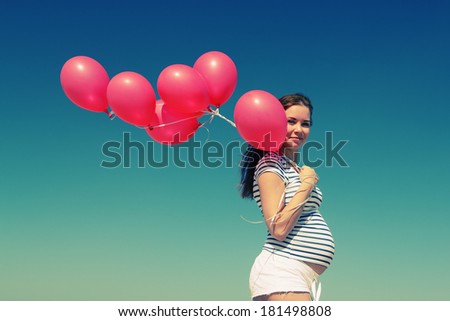 young pregnant woman holding red balloons
