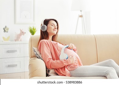 Young pregnant woman listening to music and sitting on sofa in the room