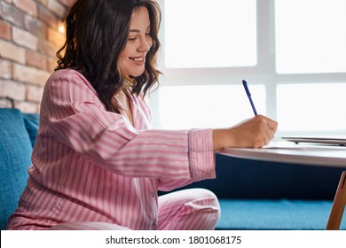 young pregnant woman making packing list for maternity hospital at home, she writes notes in diary, expect baby. sit on sofa in pajamas. new life