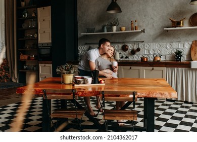 A young pregnant woman and a man in love hug and have breakfast sitting at the dining table in the kitchen in a cozy house. Expectant parents spend time together while waiting for a child.  - Powered by Shutterstock