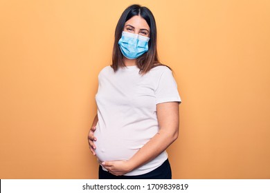 Young pregnant woman mother to be wearing protection mask for coronavirus disease with a happy and cool smile on face. Lucky person.