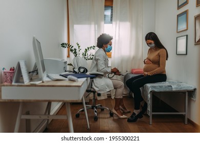 Young Pregnant Woman On A Visit To Doctor. Wearing Protective Masks During Corona Virus Epidemic.