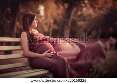 The young pregnant woman in red dress with a bouquet of wild daisies walks in the park by the lake. Riverside. Young pregnant woman walking outdoor