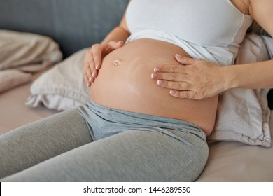 Young pregnant woman rubbing moisturising cream on her belly to moisturise her skin and reduce the possibility of stretch marks after childbirth