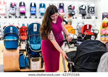 Young pregnant woman in shop of children's goods. The choice for a baby stroller